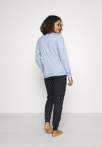 Lichtblauwe top met lange mouwen en een ronde halslijn, gecombineerd met zwarte broek tot de enkels met kleine witte hartjespatronen.