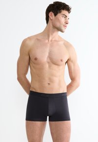 Boxer in cotone nero con una cintura comoda che presenta il nome del marchio. Il tessuto ha una texture liscia e un design aderente.