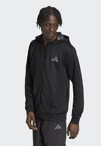 Svart zip-up hoodie i smidig tyg med en grå logotyp på bröstet, långa ärmar och en huva med mönstrad foder.