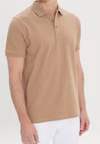 Polo beige en coton texturé, avec un col, une patte de boutonnage à trois boutons et des manches courtes avec des poignets côtelés.