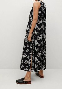 Černé květinové maxi šaty s bílými a modrými květy, s volným střihem, bočními rozparky a hladkým materiálem. Spárované s černými dřeváky.