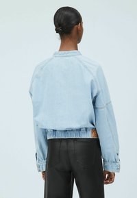 Chaqueta de mezclilla azul claro, cortada y con cintura fruncida, mangas amplias y una etiqueta con la marca "PEPE JEANS" visible en la parte de atrás.