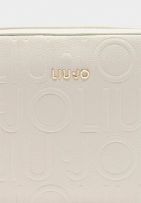 Bijela kožna torbica s utisnutim logotipom "LIUJO" i kružnim uzorcima. Ima glatku teksturu i zlatne metalne detalje.