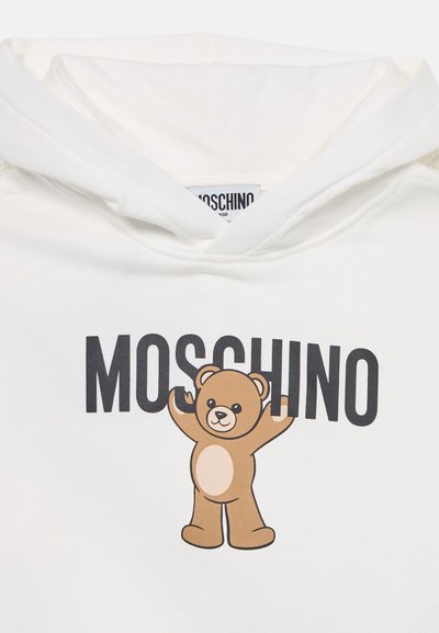 Haut à capuche blanc avec un ours en cartoon marron aux bras levés et le texte "MOSCHINO" en-dessous en lettres noires en gras. Tissu doux, design sur le devant.