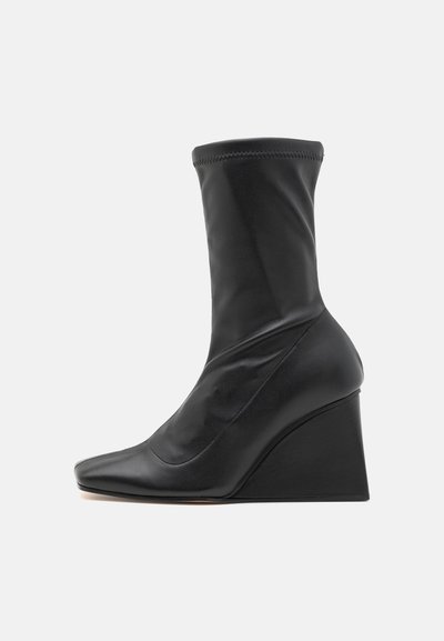 Botine negre din piele, cu toc wedge, cu un design care se fixează pe gleznă, vârf ascuțit, textură netedă și un toc sculptat distinctiv.
