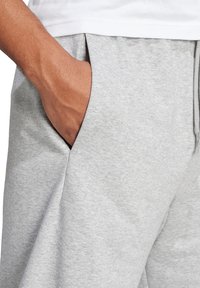Pantalon de survêtement gris avec une poche latérale, fabriqué en tissu en coton mélangé doux, présentant une coupe décontractée et une texture subtile.