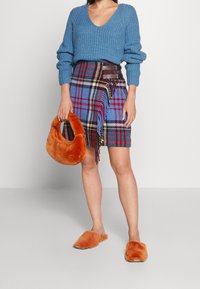 Sininen neulottu villapaita V-kauluksella, ruutuhame sinisessä, punaisessa ja keltaisessa, oranssi tekoturkislaukku ja siihen sopivat tossut.