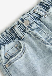 Hellblaue Jeanshose mit gesammeltem elastischem Bund, Gürtelschlaufen, Metallknopf und sichtbarer Fronttasche mit Nahtdetails.