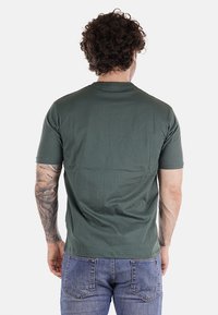 T-shirt verde khaki a maniche corte realizzato in cotone morbido, con colletto rotondo e una texture liscia, abbinato a jeans blu.