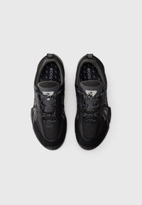 Un par de zapatos deportivos de laceado negro y gris con plantillas estampadas sobre un fondo blanco, mostrados desde arriba.