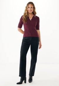 Bordový pletený polo top se zvlněným lemem a bílým lemem, zkombinovaný s černými rovnými džíny a černými kotníkovými botami na podpatku.