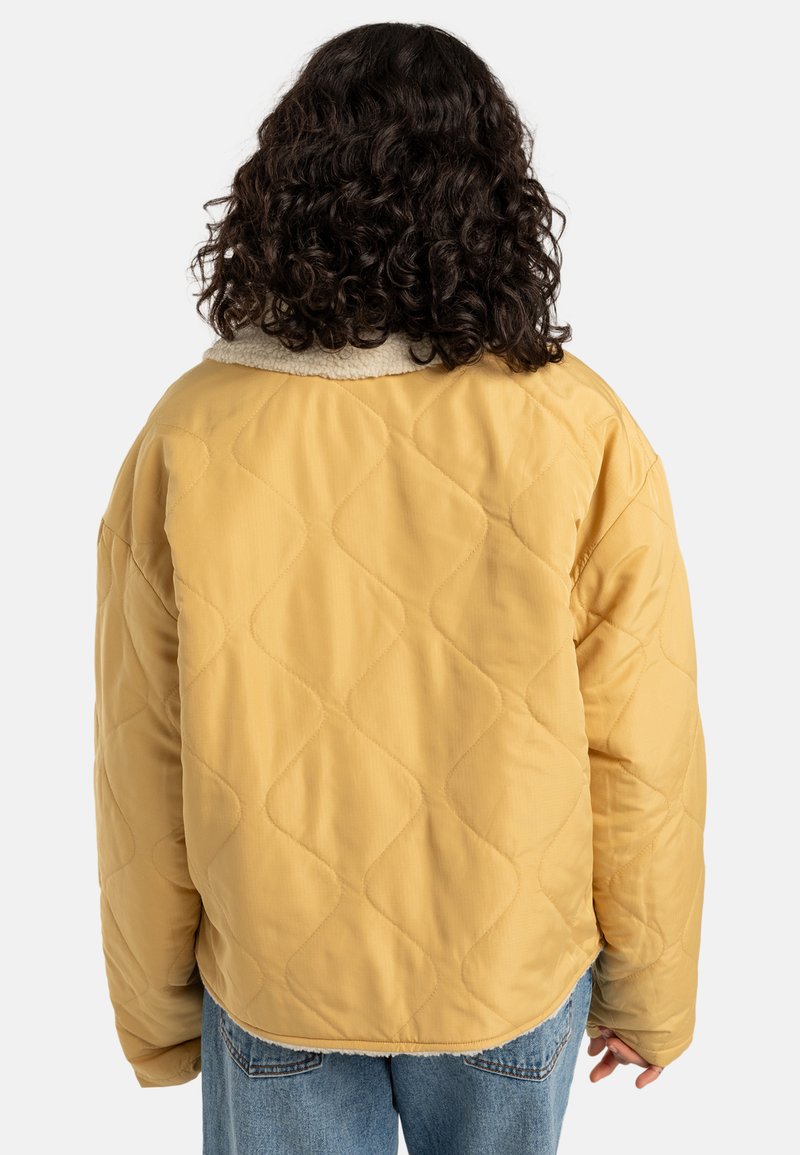 Gepolsterte gelbe Jacke mit einem weichen beigen Lammfellkragen. Übergroße Form und glatte Textur. Rückansicht, gewellter Saum.