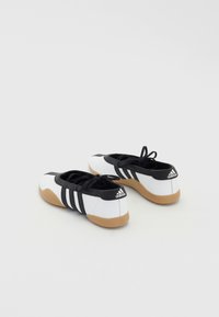 Sapatilhas de desporto em preto e branco com parte superior em têxtil, sola em borracha, três riscas pretas e um design de bico padrão.
