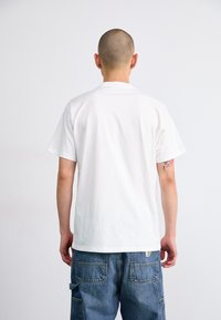 White cotton T-shirt with short sleeves and a relaxed fit, paired with blue denim cargo pants featuring large pockets and visible stitching.