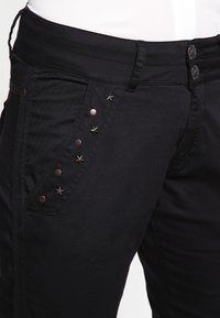 Svarta denimbyxor med en figurnära design, stjärnformade dekorstjärnor och dubbel knappstängning vid midjan.