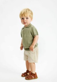Pikétröja i dämpad grön, korta ärmar; ljusbeiga shorts; bruna lädersandaler med remmar; minimalistisk design, slät textur.