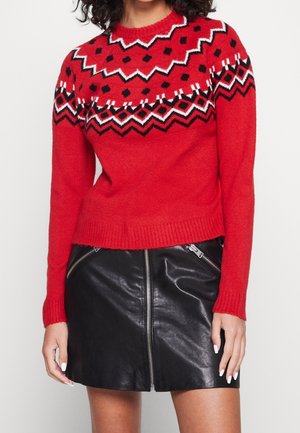 Maglione rosso lavorato a maglia con scollatura decorata, caratterizzato da motivi geometrici in bianco e nero, abbinato a una mini gonna in pelle nera con zip.
