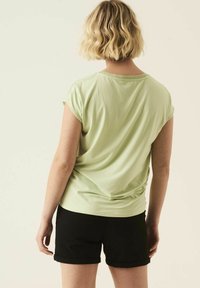 Camisa de manga corta verde claro con un corte holgado y textura suave, combinada con pantalones cortos negros doblados. Diseño simple y casual.