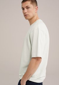 Heled roheline puuvillane t-särk lühikeste varrukatega, mugav lõige, ümmargune kaelus ja õmblusdetailid. Kandnud tumesiniste pükste ja mudel on külje pealt.