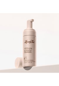 Mousse autobronzante Loving Tan 8 heures en teinte moyenne, flacon à pompe avec bouchon placé derrière sur une surface claire.