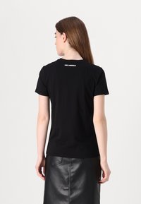 Svart bomull T-skjorte med korte ermer, rund hals, med en liten hvit "KARL LAGERFELD"-logo på baksiden. Glatt tekstur.