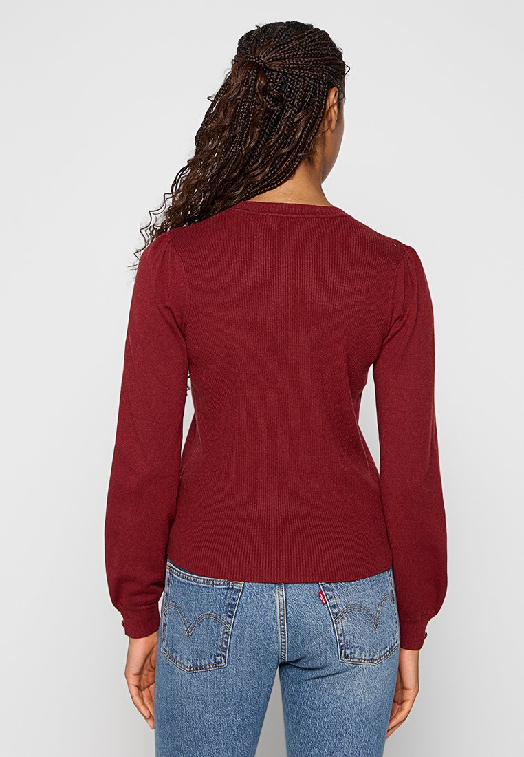 Bordeaux ribbeltrui met aangezette lange mouwen en een getailleerde taille, van achteren getoond tegen een neutrale achtergrond.