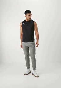 Svart ermeløs treningsgenser og grå joggebukser. Buksene har sidelommer og elastiske mansjetter. Brukt med hvite joggesko.