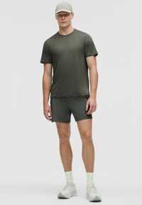 Ensemble de t-shirt et shorts de sport vert, fabriqué en tissu léger. Présente un col rond et des manches courtes, associé à des chaussettes vert clair et des chaussures grises.