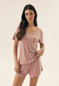 Jasnoróżowa koszulka z krótkim rękawem i dekoltem w serek, zestawiona z pasującymi szortami. Materiał wydaje się miękki i gładki, o swobodnym kroju.