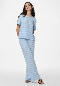 Gaiši zils adīts top un bikses komplekts ar teksturētām horizontālām svītrām. Brīvs piegriezums, apaļa kakla izgriezums, īsas piedurknes un platas bikses.