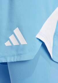 Abbigliamento sportivo azzurro chiaro con logo Adidas bianco. Il tessuto ha una texture liscia con un dettaglio in rete bianco.