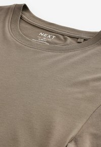 Camiseta ajustada de color verde oliva hecha de algodón suave, con cuello redondo y mangas cortas. Etiqueta visible en el cuello con el nombre de la marca "NEXT."