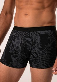 Boxer shorts noirs avec un motif subtil de feuilles de fougère noires. Fabriqués en tissu doux, avec une taille élastique portant une marque.