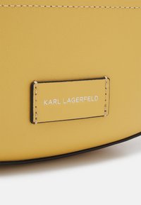 Borsa gialla in pelle con una superficie liscia, caratterizzata da un bordo nero e un'etichetta rettangolare che mostra "KARL LAGERFELD" in lettere bianche.