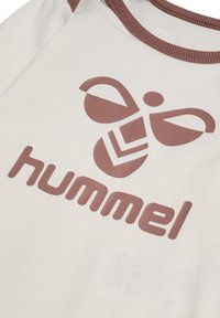 Weißes Baumwoll-T-Shirt mit einem großen braunen Bienenlogo und dem Text "hummel" in passender Farbe, ergänzt durch einen braunen gerippten Ausschnitt und Details.