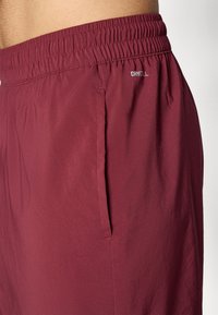 Burgunderrote Shorts mit einem elastischen Taillenbund, seitlichen Taschen und dem Aufdruck "DRYCELL" auf dem Taillenbund. Glatte Textur.