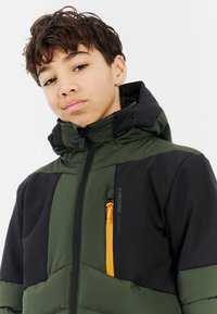 Groene en zwarte gewatteerde jas met een hoge kraag, een oranje ritszak en een verstelbare capuchon. Bevat een logo op de voorkant.