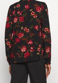 Schwarze Bluse mit langen Ärmeln, die ein florales Muster in Rot, Pink und Grün zeigt, mit zarten Akzenten, lockerer Passform und knöpfbaren Manschetten.