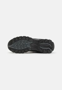 Suela de zapatilla deportiva negra con un patrón de relieve texturizado. Presenta ranuras y una sección elevada para ofrecer tracción. Fabricada con materiales de goma y sintéticos.