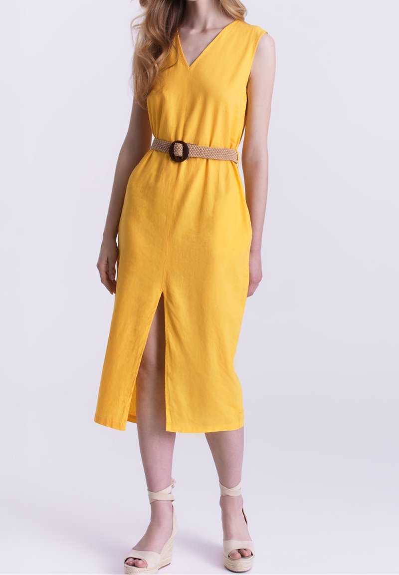 Robe jaune sans manches avec un col en V et une fente latérale, cintrée avec une ceinture tressée beige et accompagnée de sandales compensées beige clair.