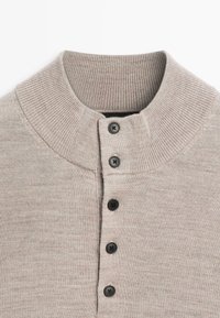 Maglione a maglia beige chiaro con colletto alto a costine e una fila verticale di cinque bottoni neri sul davanti.