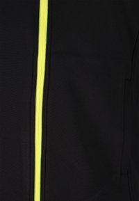 Schwarze Jacke mit einem auffälligen neongelben Reißverschluss an der Vorderseite, aus glattem Stoff mit einer strukturierten Oberfläche.