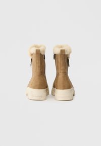 Brązowe zamszowe botki do kostki z puszystym, kremowym kołnierzem z sztucznego futra, bocznymi zamkami błyskawicznymi oraz grubą, teksturowaną białą podeszwą.