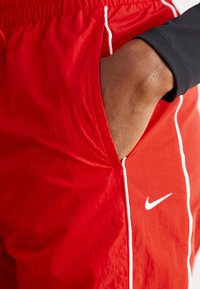 Rdeče kratke hlače z belim obrobljanjem in Nike logotipom, narejene iz lahkega materiala, z bočnim žepom in elastičnim pasom.