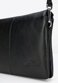 Czarna skórzana kopertówka o fakturowanej powierzchni, z akcentem srebrnej metalowej ozdoby i wytłoczonym logo. Prosty, prostokątny kształt.