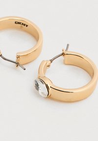 Σκουλαρίκια κρίκοι σε χρυσό χρώμα με στρογγυλό διάφανο στρας, λεία υφή και ασφαλές μεταλλικό κούμπωμα.