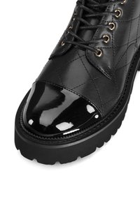 Černé kožené kotníkové boty s prošívaným vzorem, lesklou lakovanou špičkou, kulatými šňůrkami a silnou, texturovanou gumovou podrážkou.