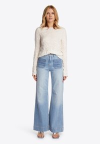 Lichtgevoerd crèmekleurig longsleeve tshirt gecombineerd met hoge taille, wijd uitlopende vervaagde denim jeans en metallic sandalen.
