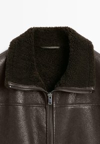 Mørkebrun shearlingjakke med struktureret læder yderside, blød, fluffy krave og central sølvlynlås.