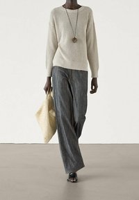 Pull en tricot gris clair avec une texture côtelée, associé à un jean en denim foncé à coupe ample et un sac fourre-tout tissé, agrémenté d'un long collier.